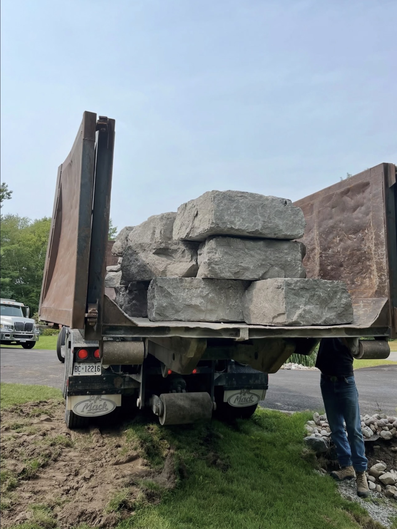 Dump truck box raised with a load of grey armour stone blocks on a residential driveway