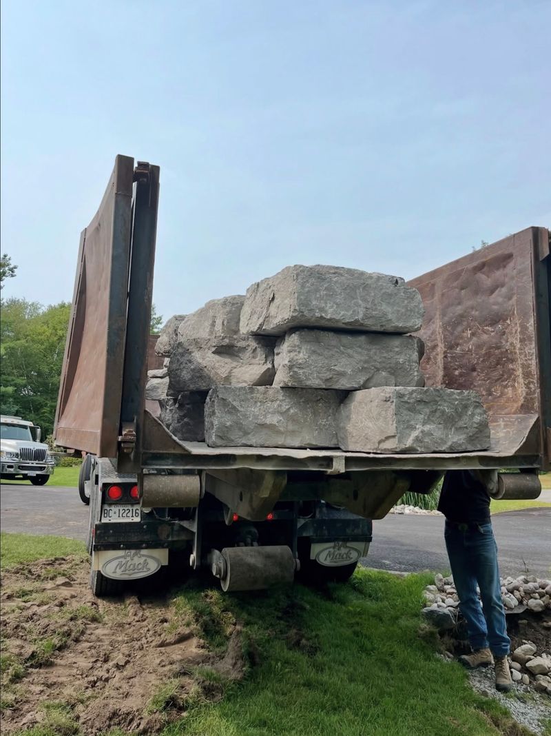 Dump truck box raised with a load of grey armour stone blocks on a residential driveway